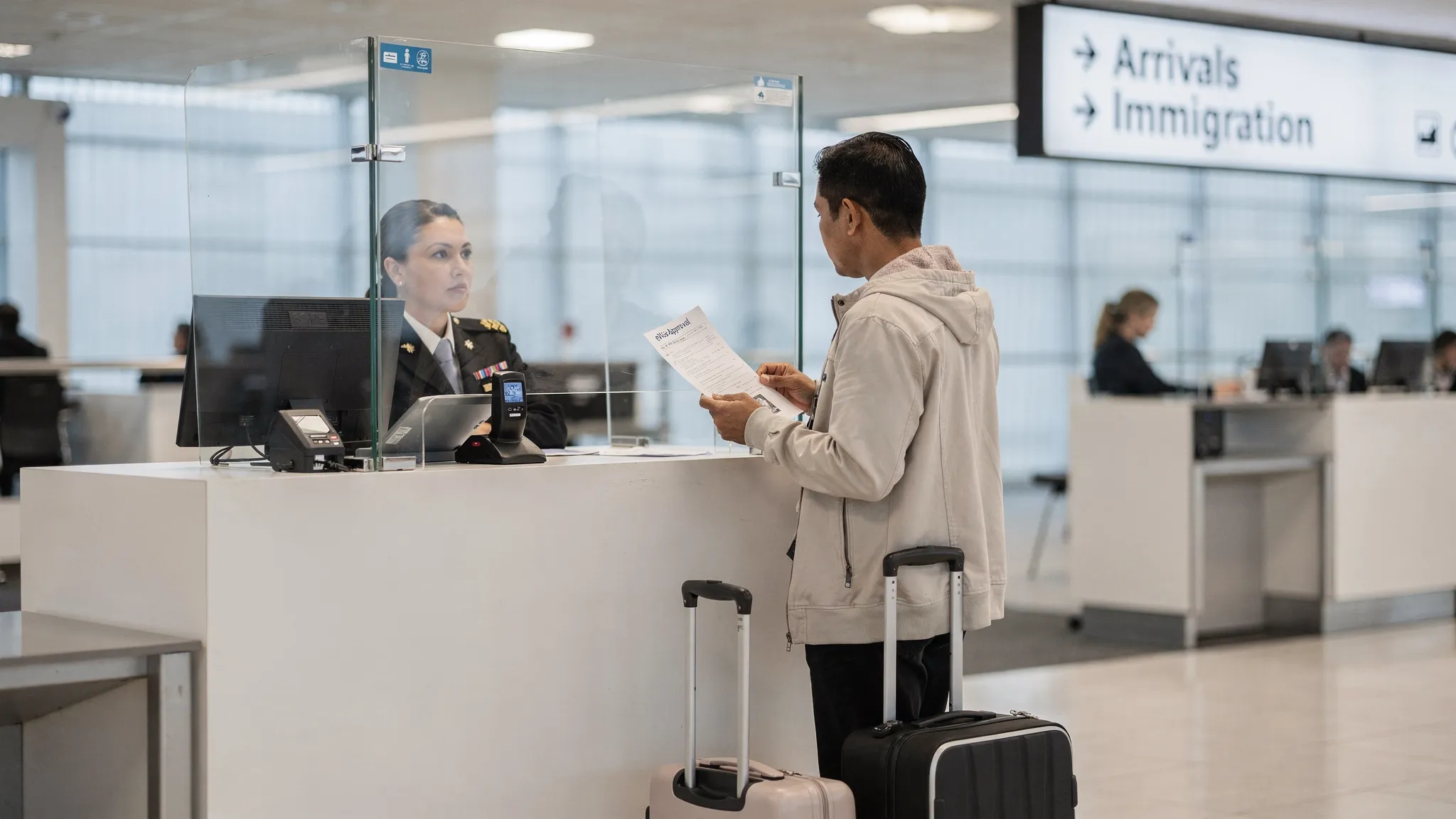 An airport immigration counter scene with a traveler handing over a passport and a printed eVisa approval page to a border officer, with a carry-on beside them and clear signage for “Arrivals Immigration.”