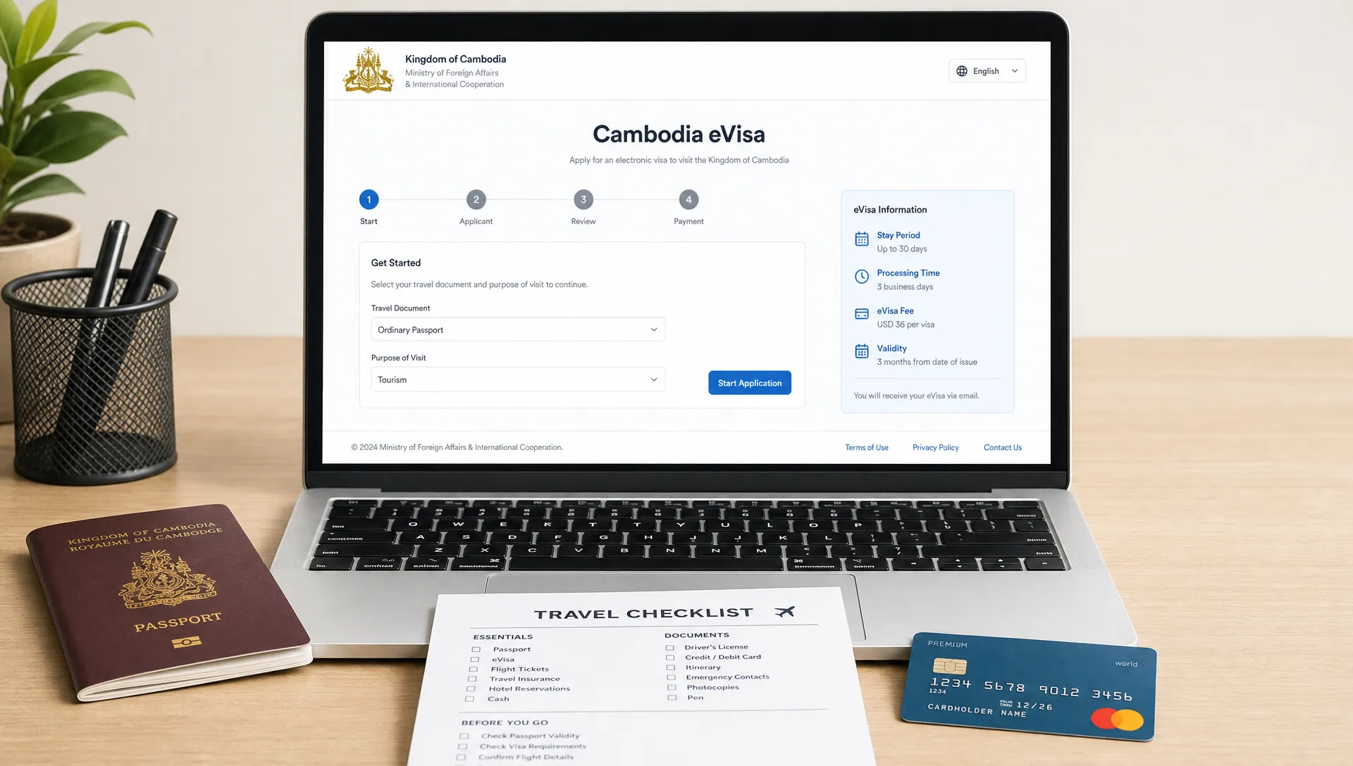 A passport, printed travel checklist, payment card, and laptop on a desk showing a front-facing generic Cambodia eVisa application page; the laptop screen faces the viewer clearly, with no objects behind the screen.